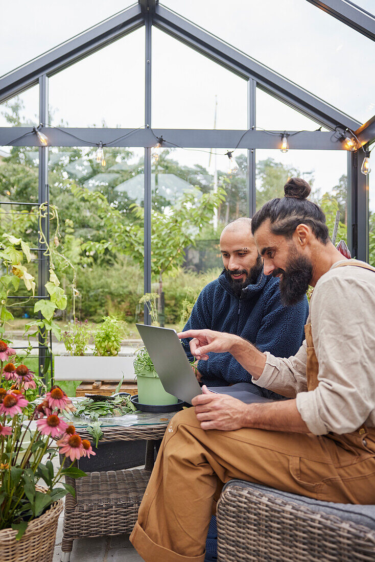 Smiling men using laptop in greenhouse