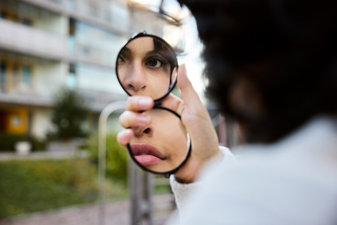 Junge Frau, die sich im Handspiegel reflektiert