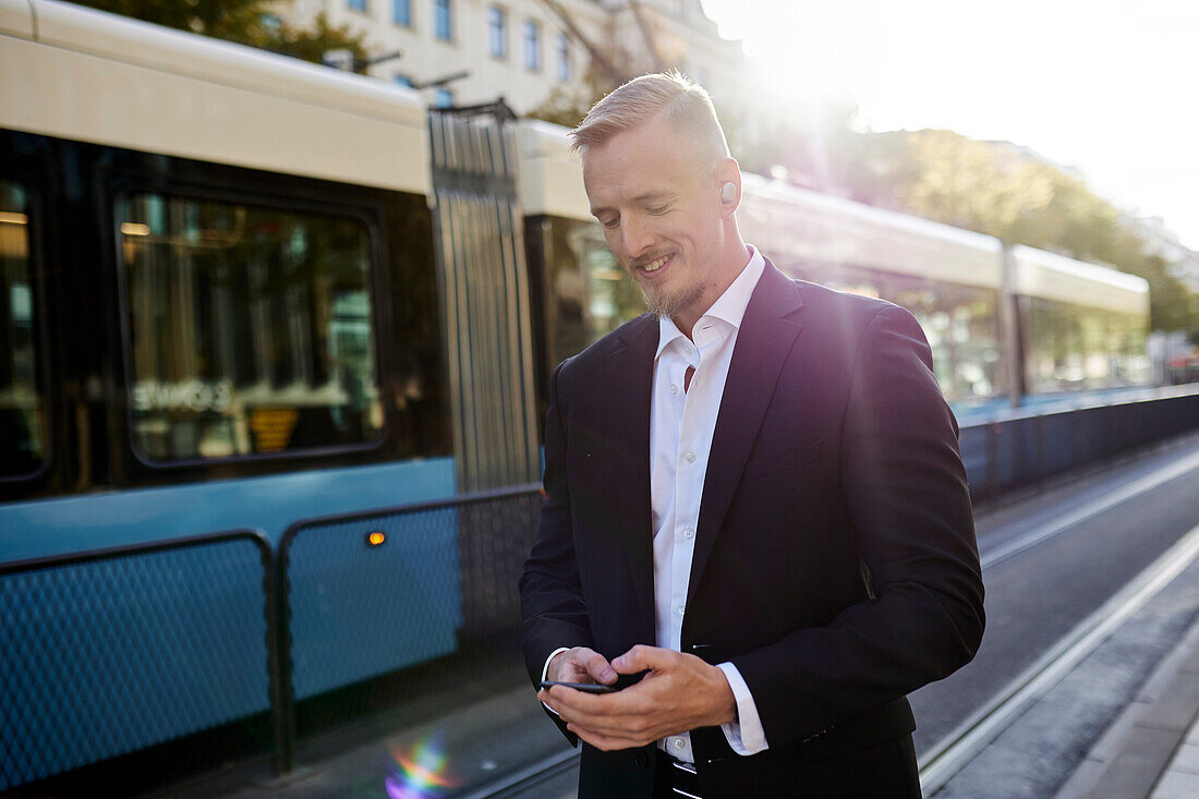 Businessman waiting at tram stop and using phone