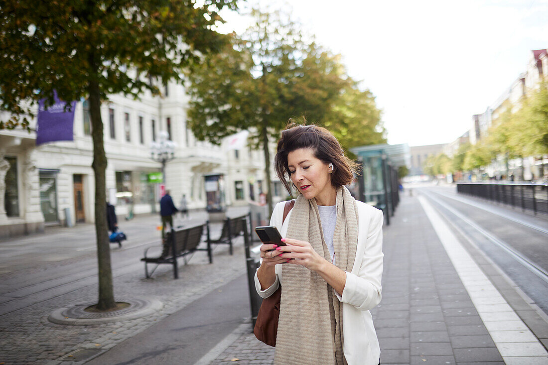 Lächelnde Geschäftsfrau, die ein Smartphone auf der Straße benutzt