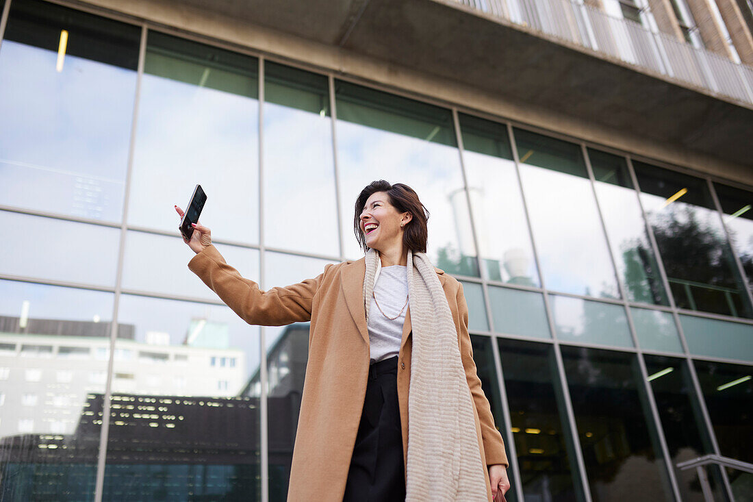 Lächelnde Geschäftsfrau, die ein Selfie vor einem Bürogebäude macht