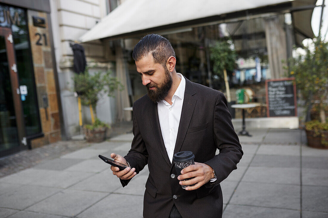 Businessman using phone and holding coffee cup in street