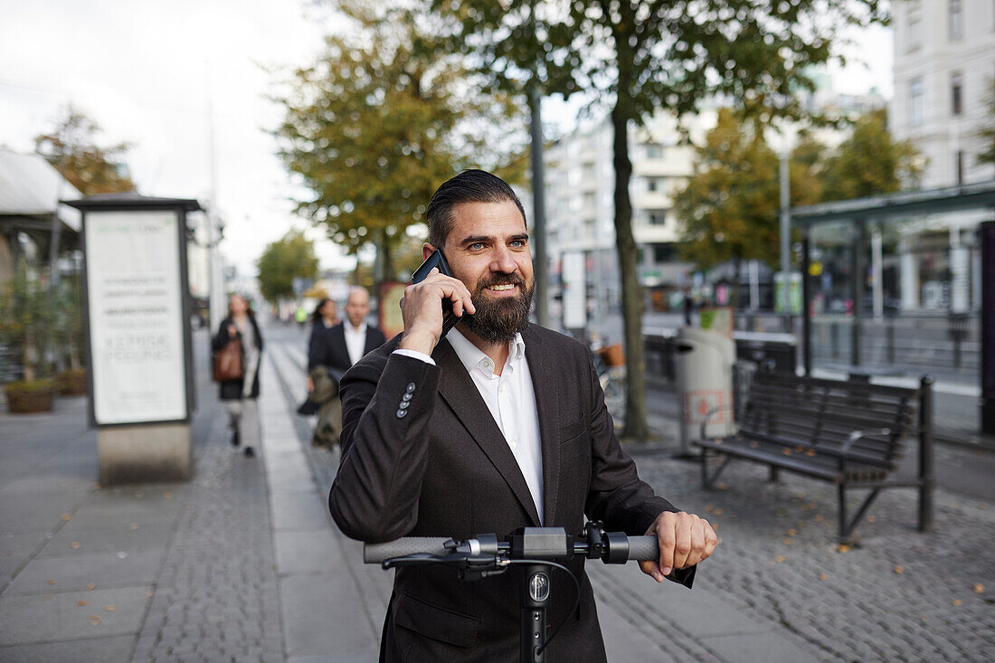 Businessman riding electric push scooter and talking on phone