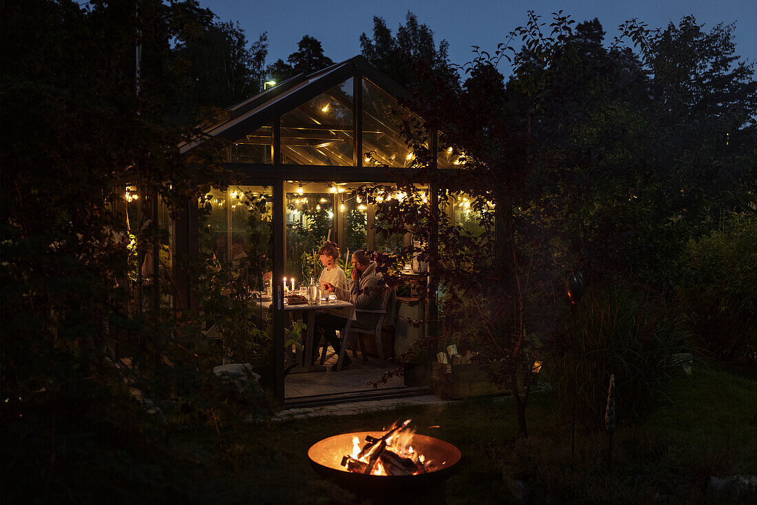 People having meal in illuminated greenhouse