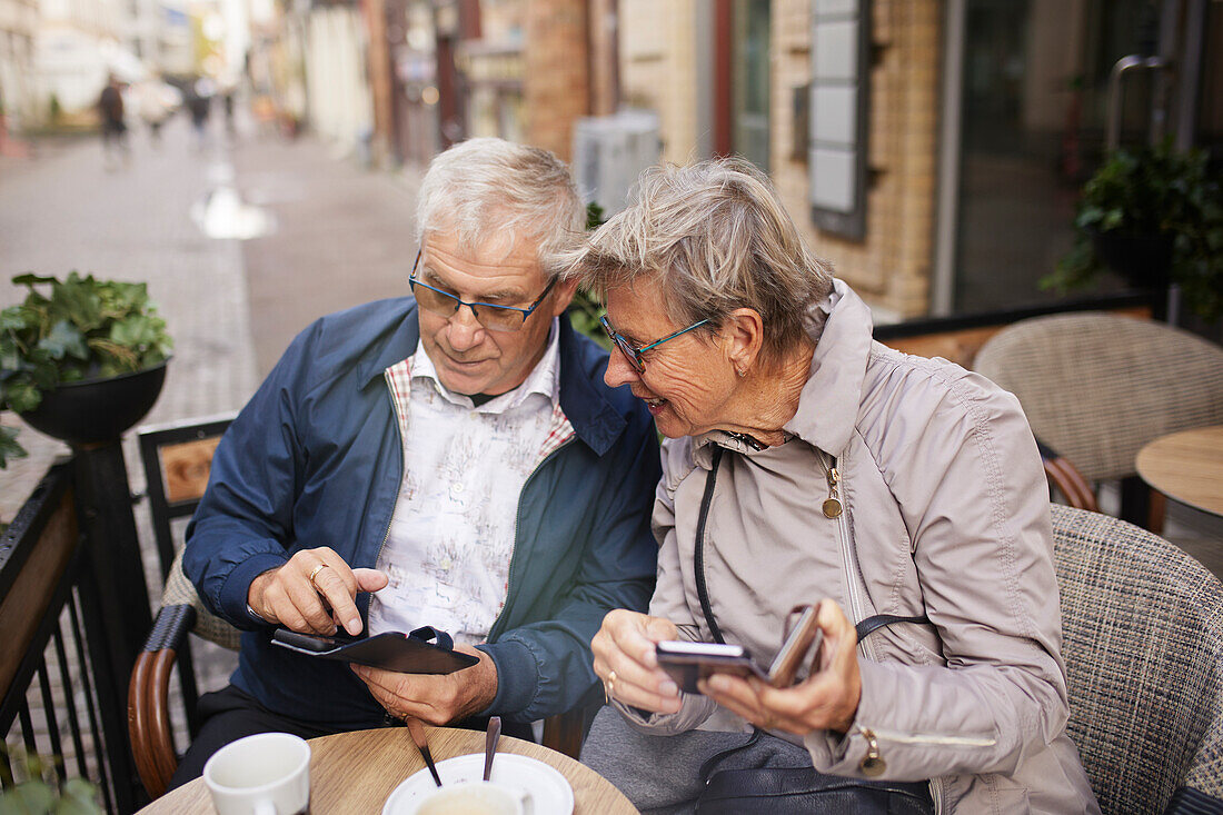 Mature couple in outdoor cafe using phones