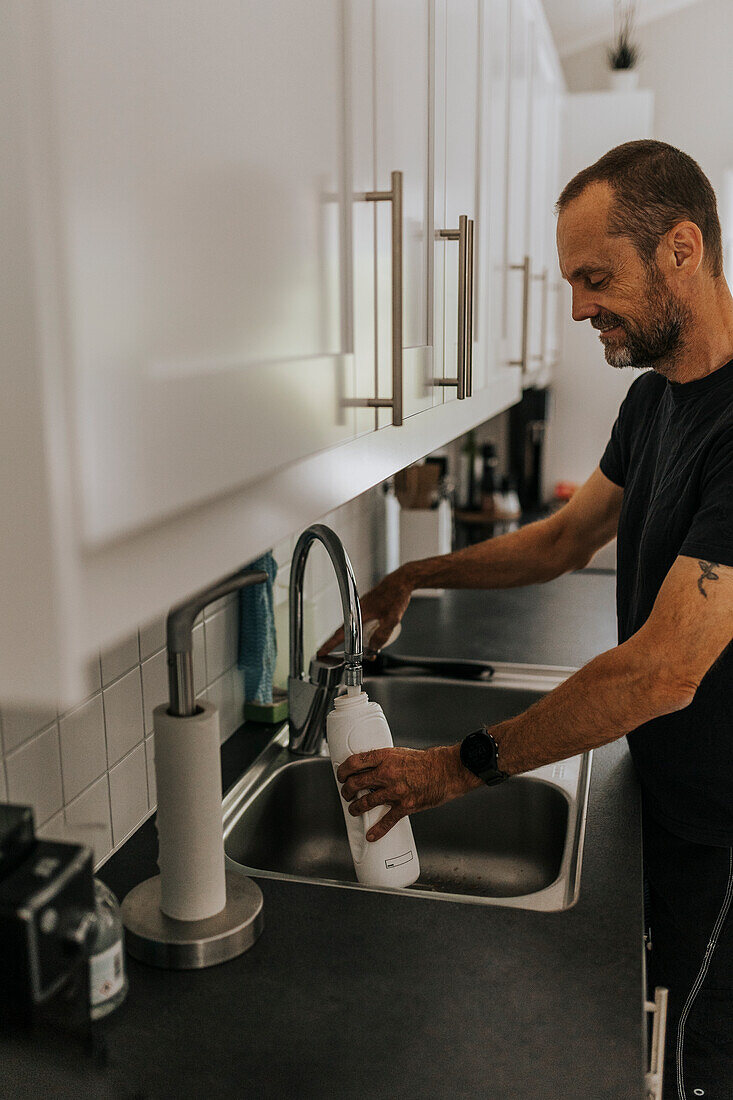 Mann füllt Wasserflasche in Küche auf