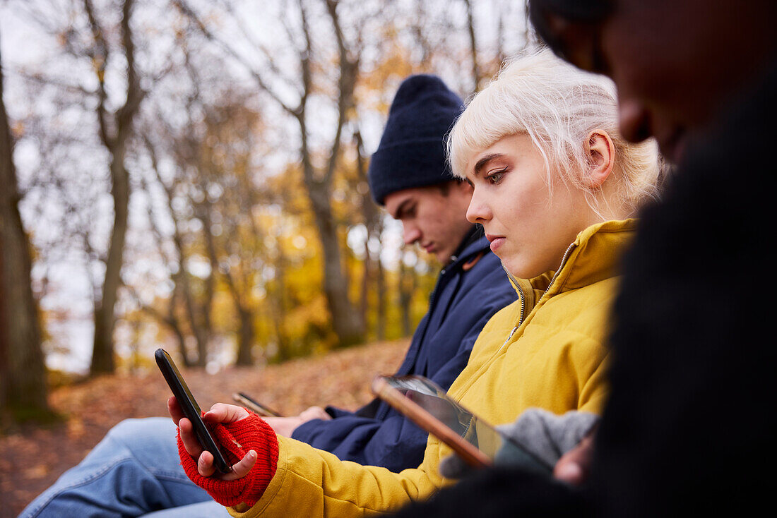 Three friends in park using smartphones