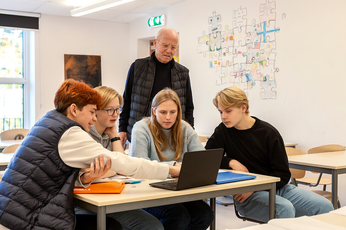 Teenage boys and teacher using laptop in classroom