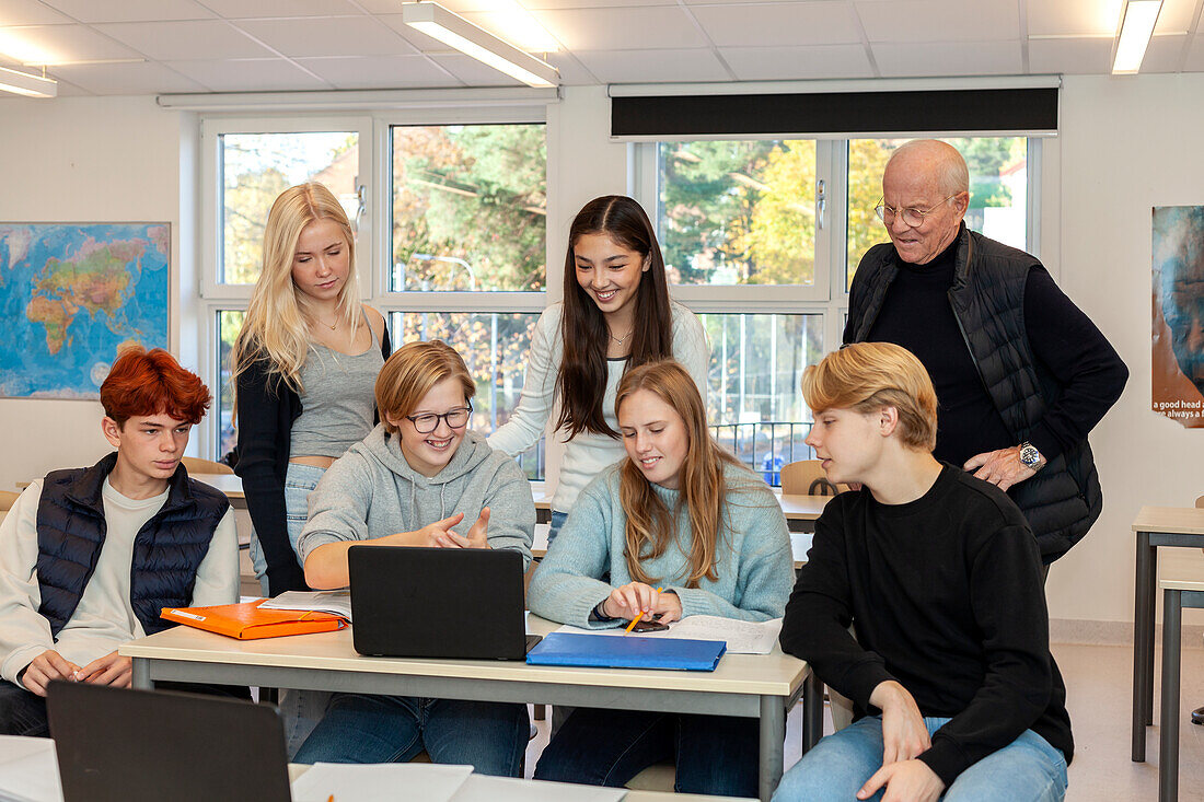 Teenage kids and teacher using laptop in classroom