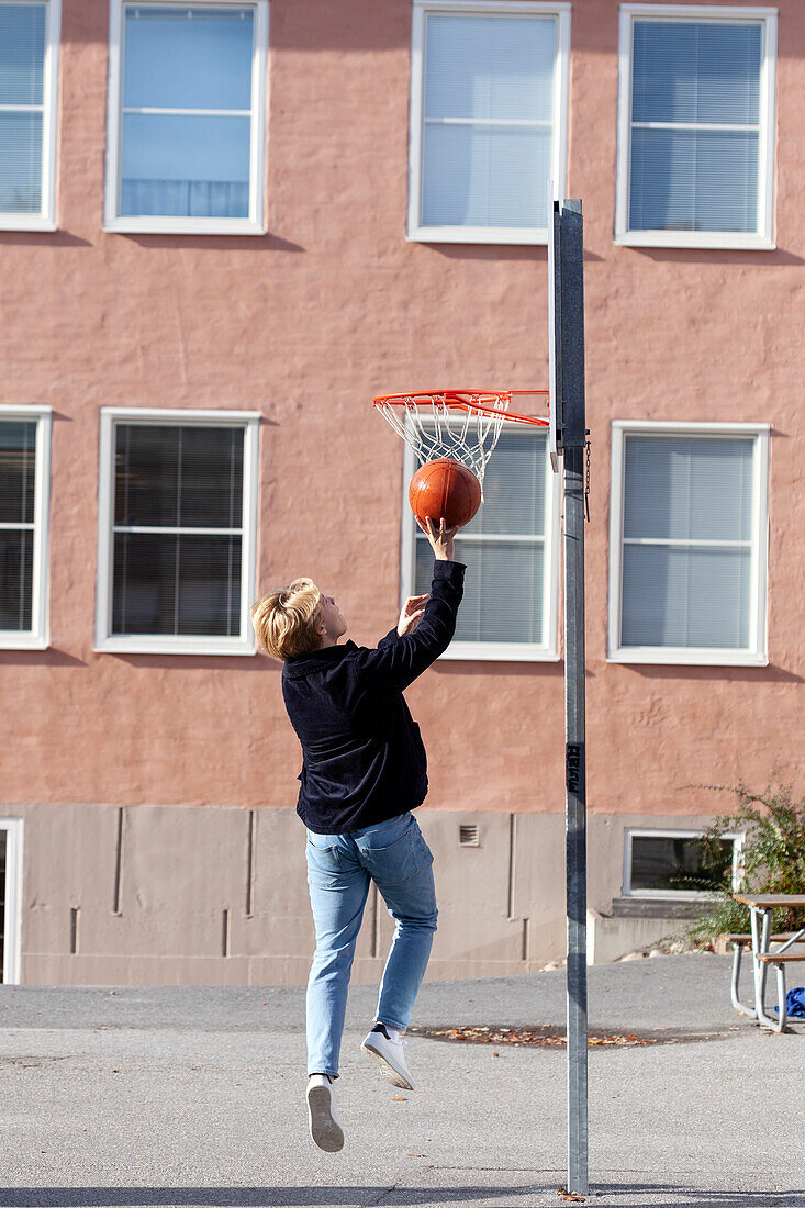 Teenage boy playing basketball in schoolyard