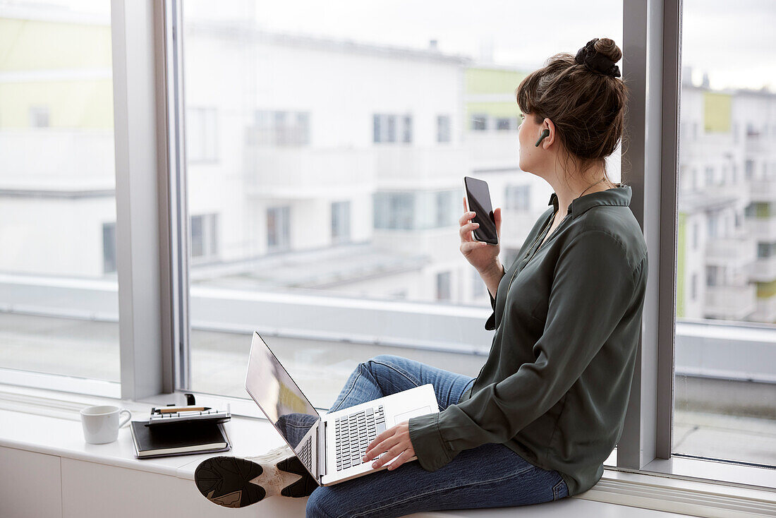 Businesswoman using laptop and phone in office