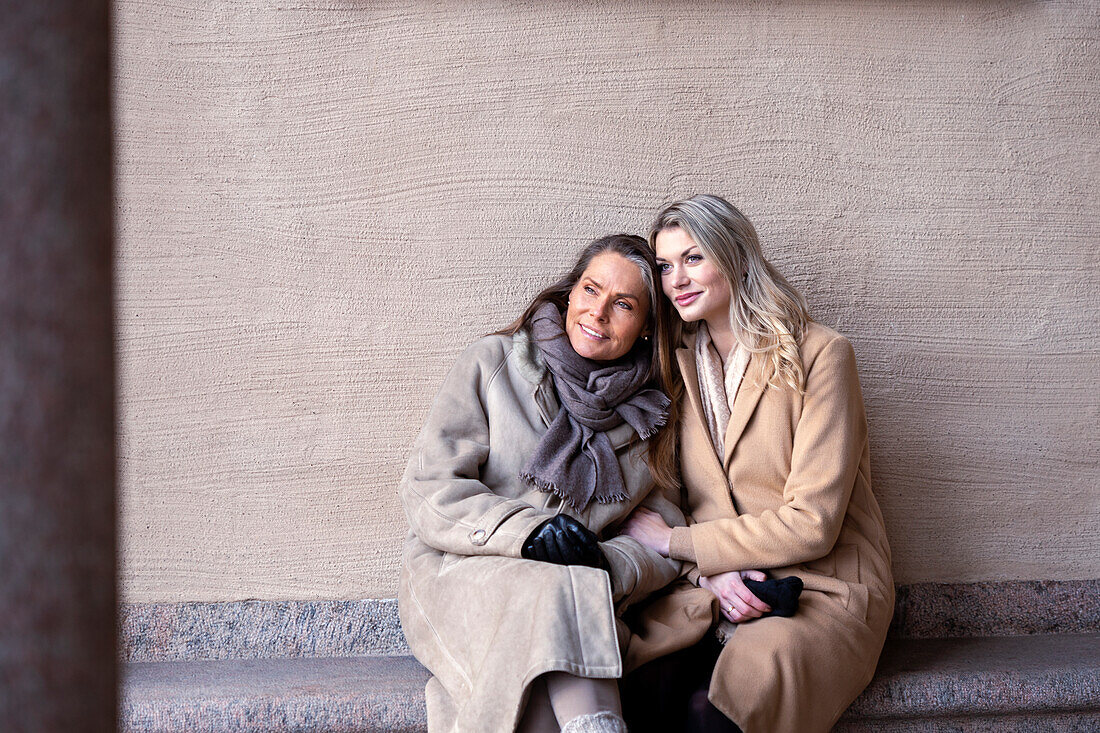 Mother with adult daughter sitting on stone bench