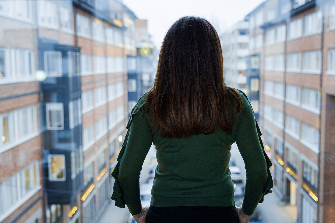 Frau blickt durch ein Fenster auf ein Wohnhaus