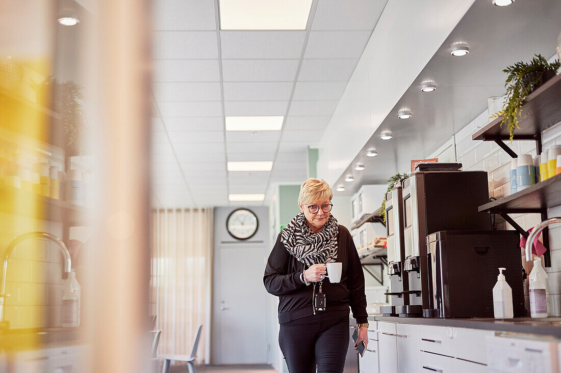 Ältere Frau macht Kaffeepause in der Büroküche