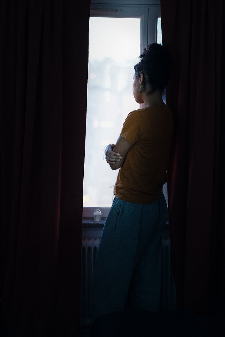 Nachdenkliche junge Frau blickt durch ein Fenster