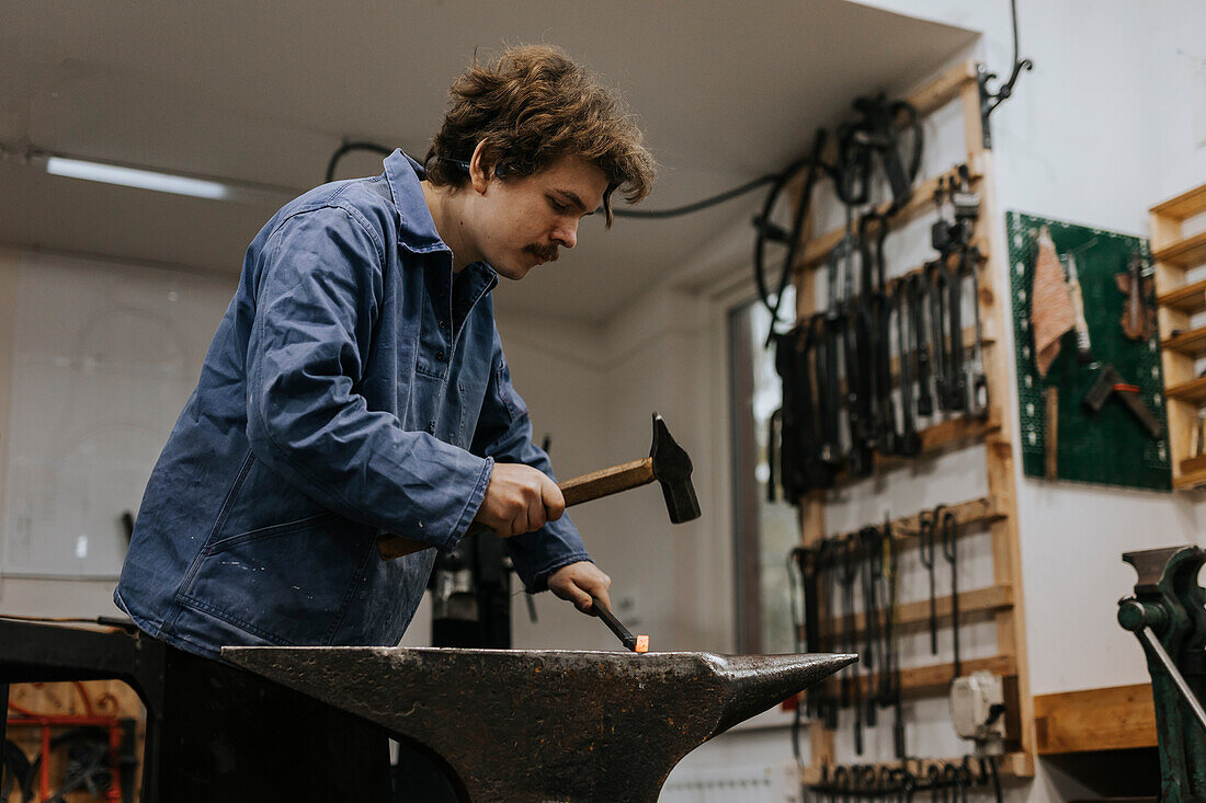 Blacksmith using hammer and anvil in workshop