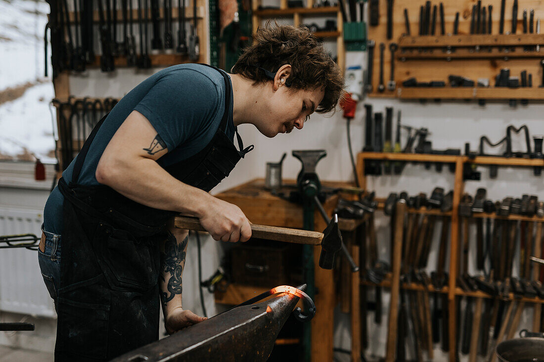 Blacksmith using hammer and anvil in workshop