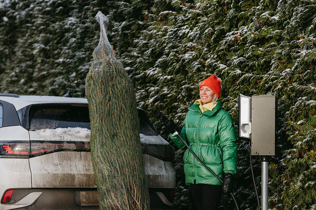 Lächelnde Frau mit Weihnachtsbaum am Auto stehend