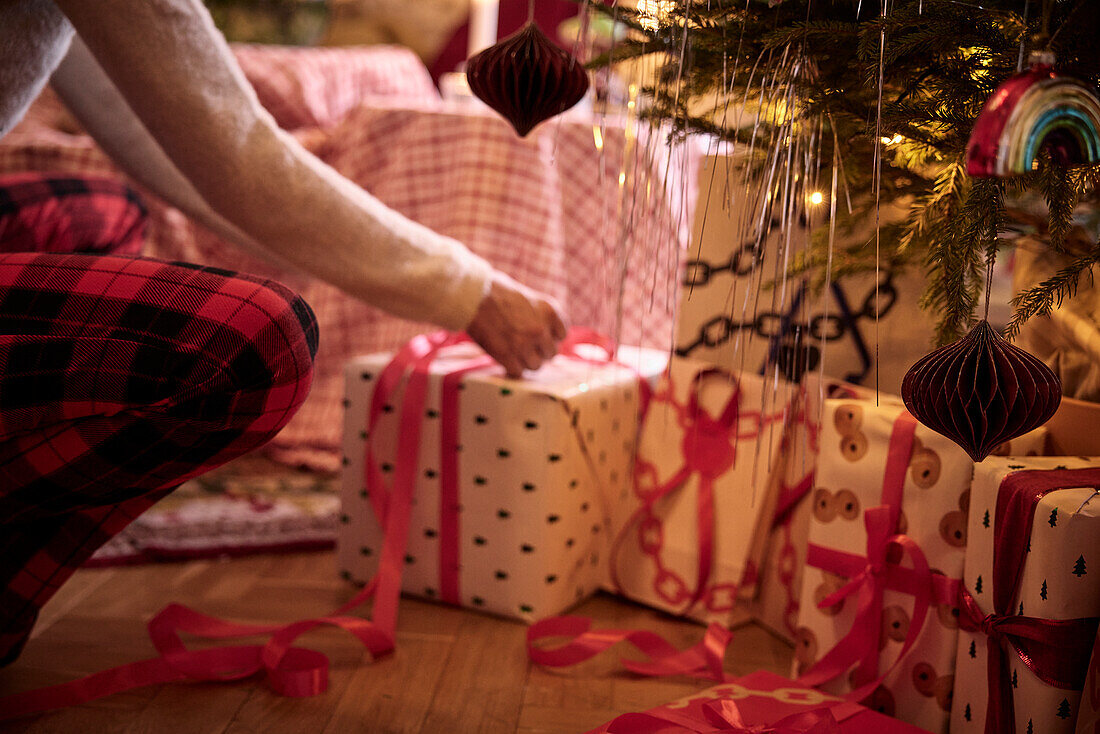 Person wrapping present under Christmas tree