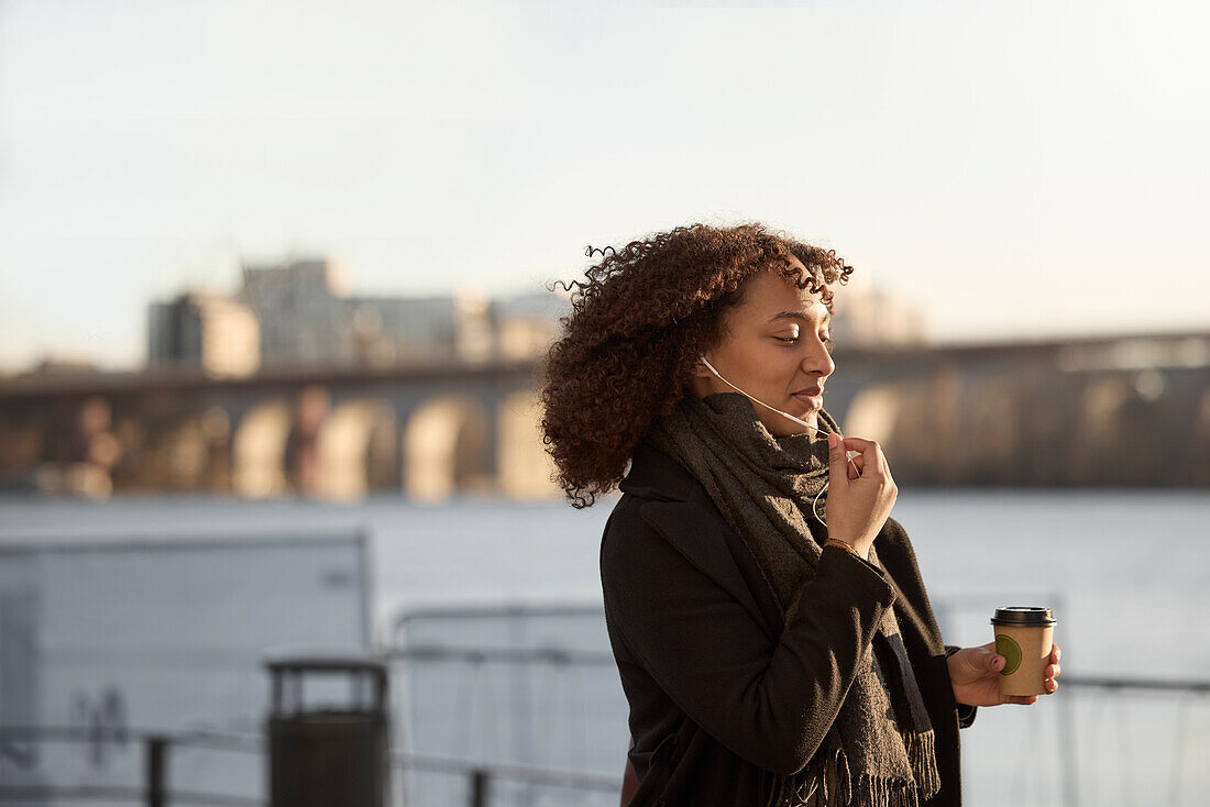 Beautiful woman with takeaway coffee walking near river