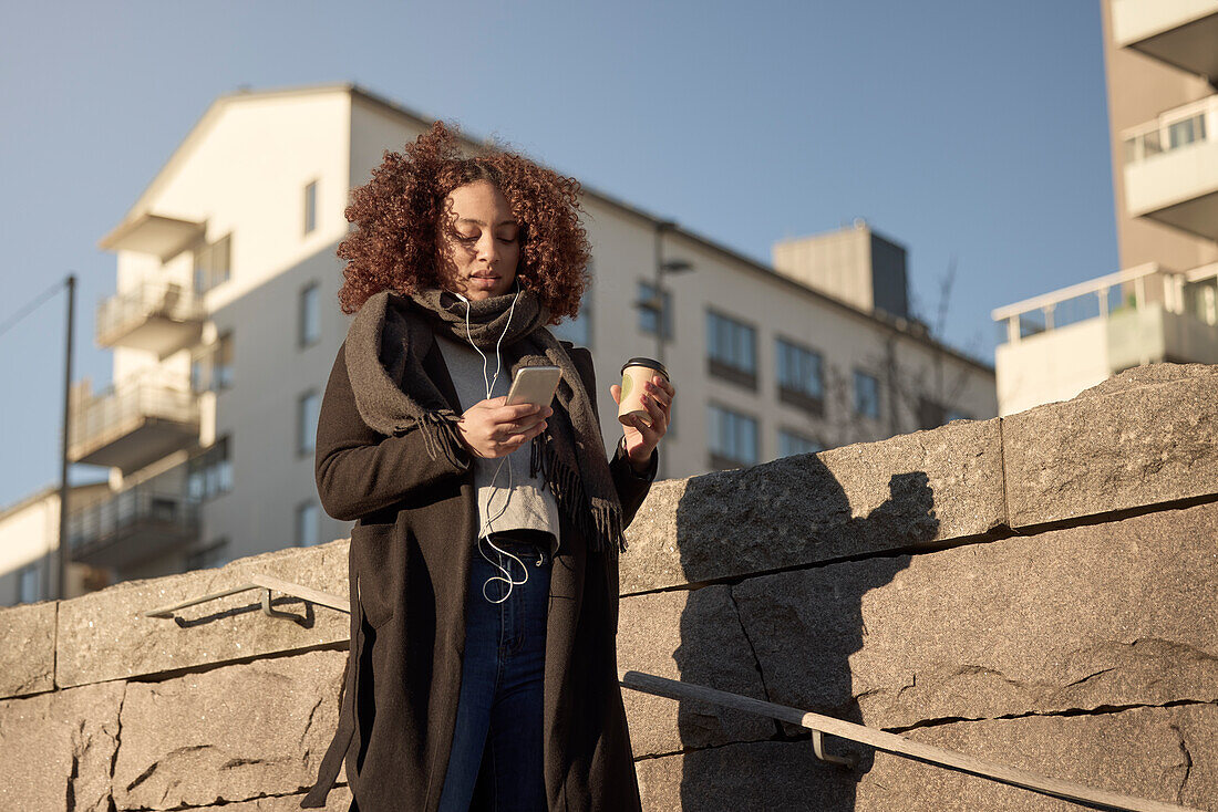 Beautiful woman with takeaway coffee and smartphone on street