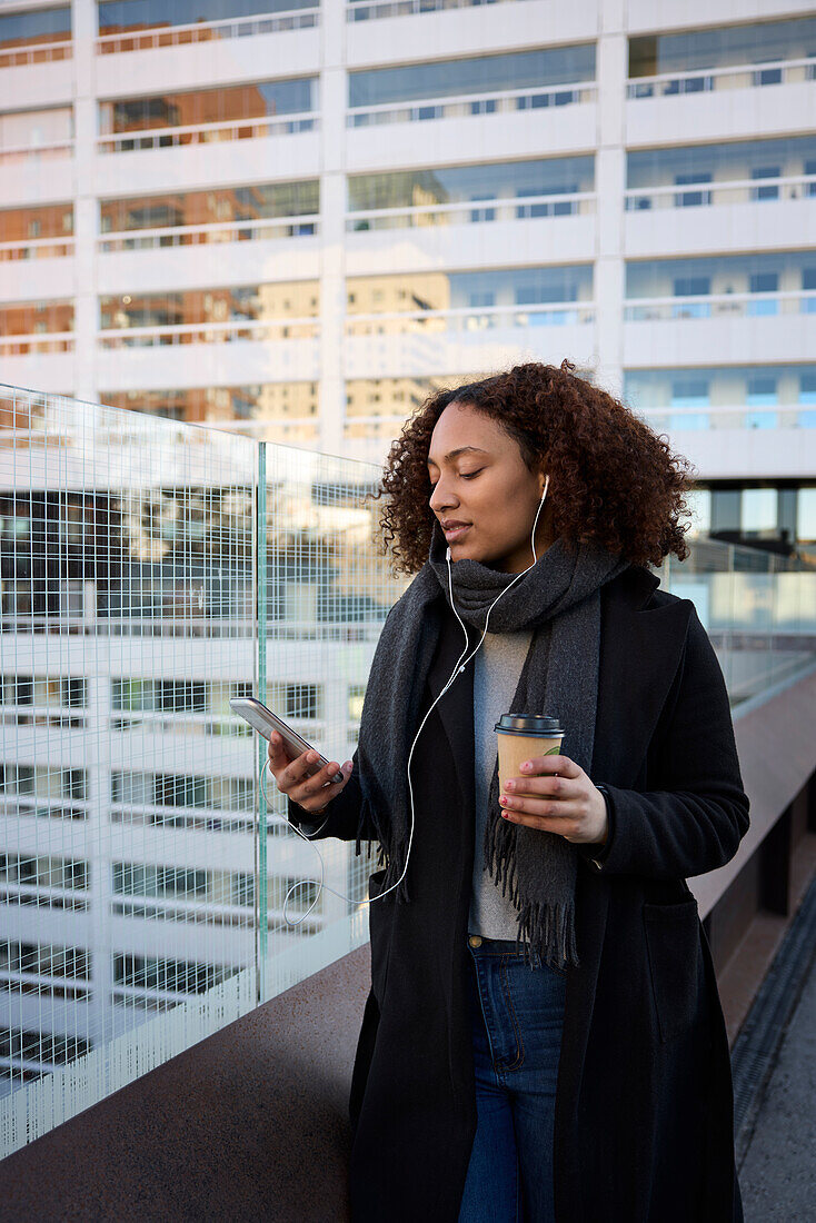 Schöne Frau mit Kaffee zum Mitnehmen und Smartphone im Stadtzentrum
