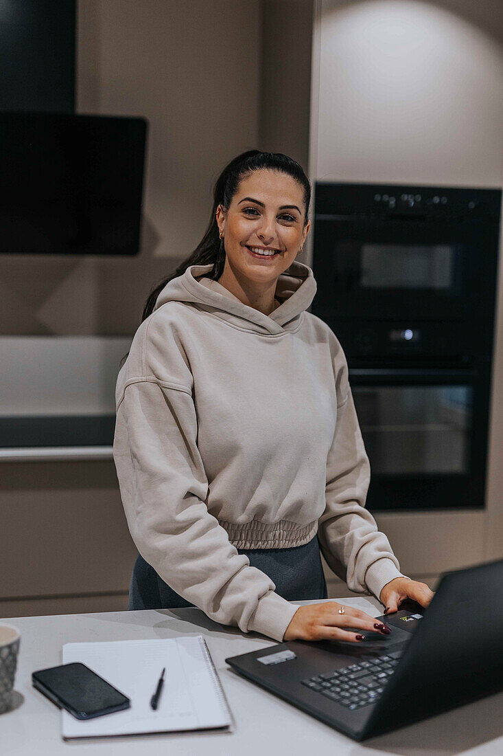 Smiling woman in kitchen using laptop