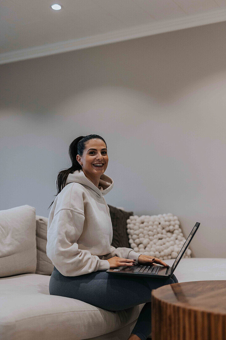 Lächelnde Frau mit Laptop auf dem Sofa