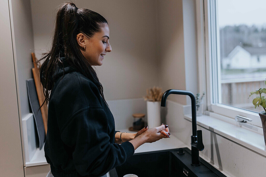 Smiling woman washing hands in kitchen