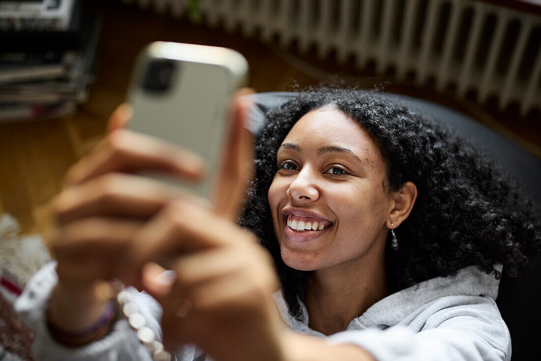Lächelnde junge Frau, die auf einem Sitzsack liegt und ein Selfie macht