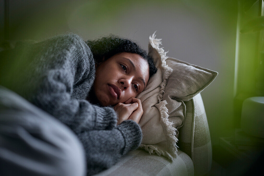 Pensive young woman lying on sofa