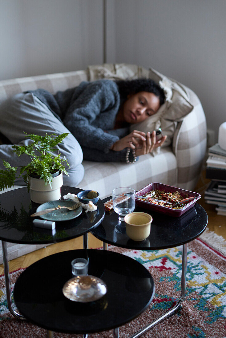 Nachdenkliche junge Frau auf dem Sofa liegend und telefonierend