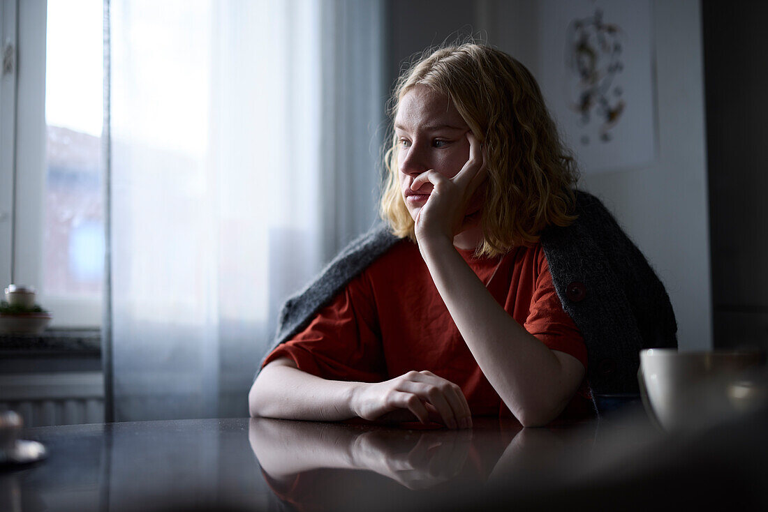 Pensive teenage girl sitting at table with hand on chin