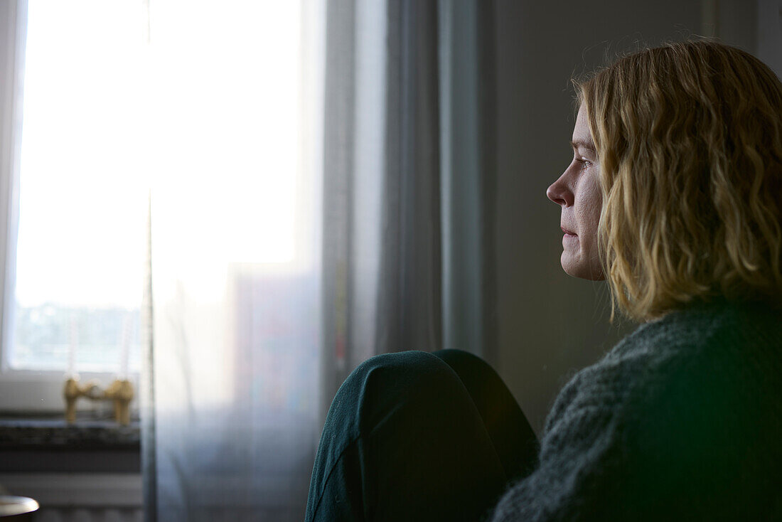 Pensive teenage girl looking through window