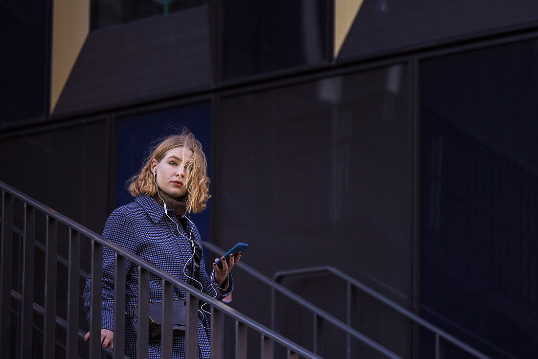 Junge Frau geht eine Treppe hinunter und hält ein Telefon in der Hand