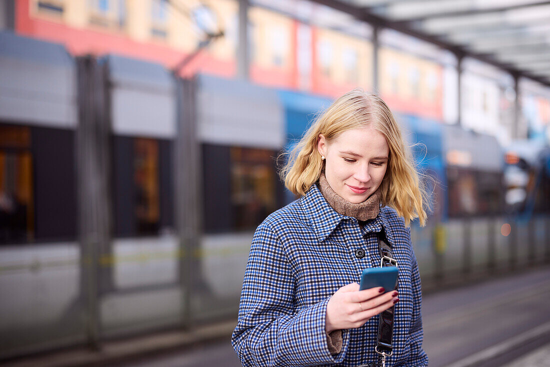 Frau mit Handy an der Straßenbahnhaltestelle