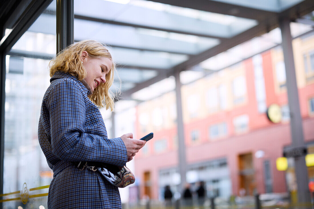 Frau telefoniert mit Handy an der Bushaltestelle