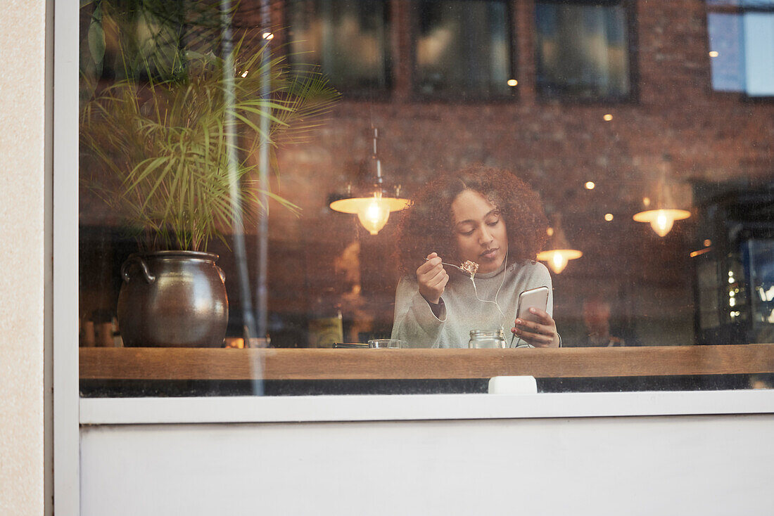 Junge Frau, die ein Handy benutzt und in einem Café isst