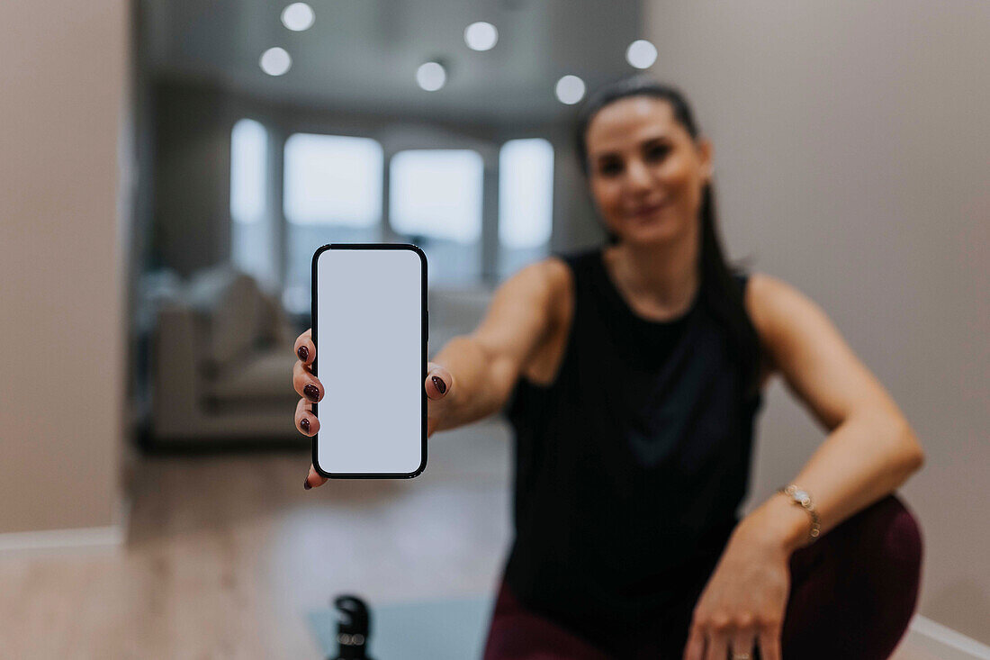 Frau zeigt Handy mit Workout-App