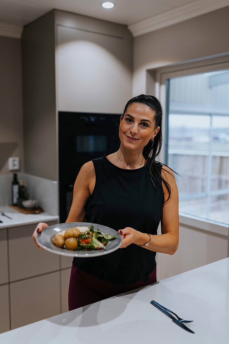 Woman holding plate with food in kitchen