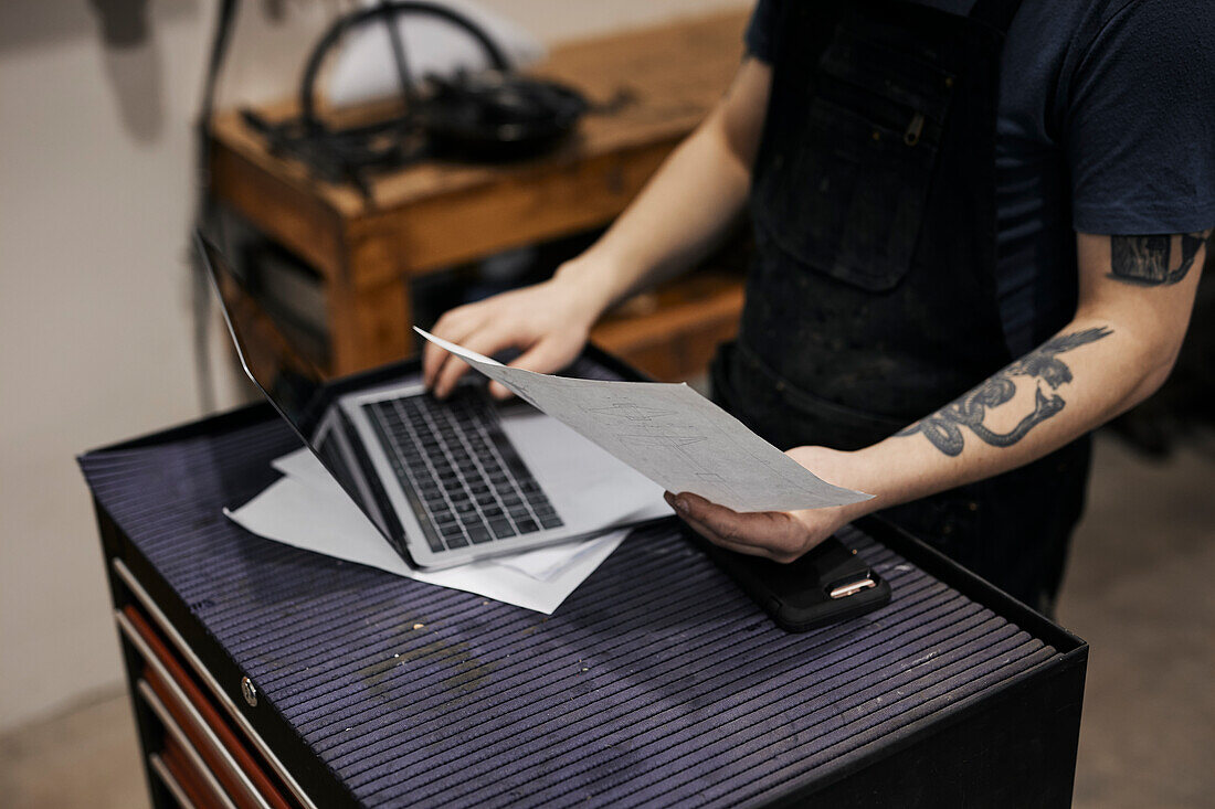 Blacksmith working with laptop and documents in his workshop