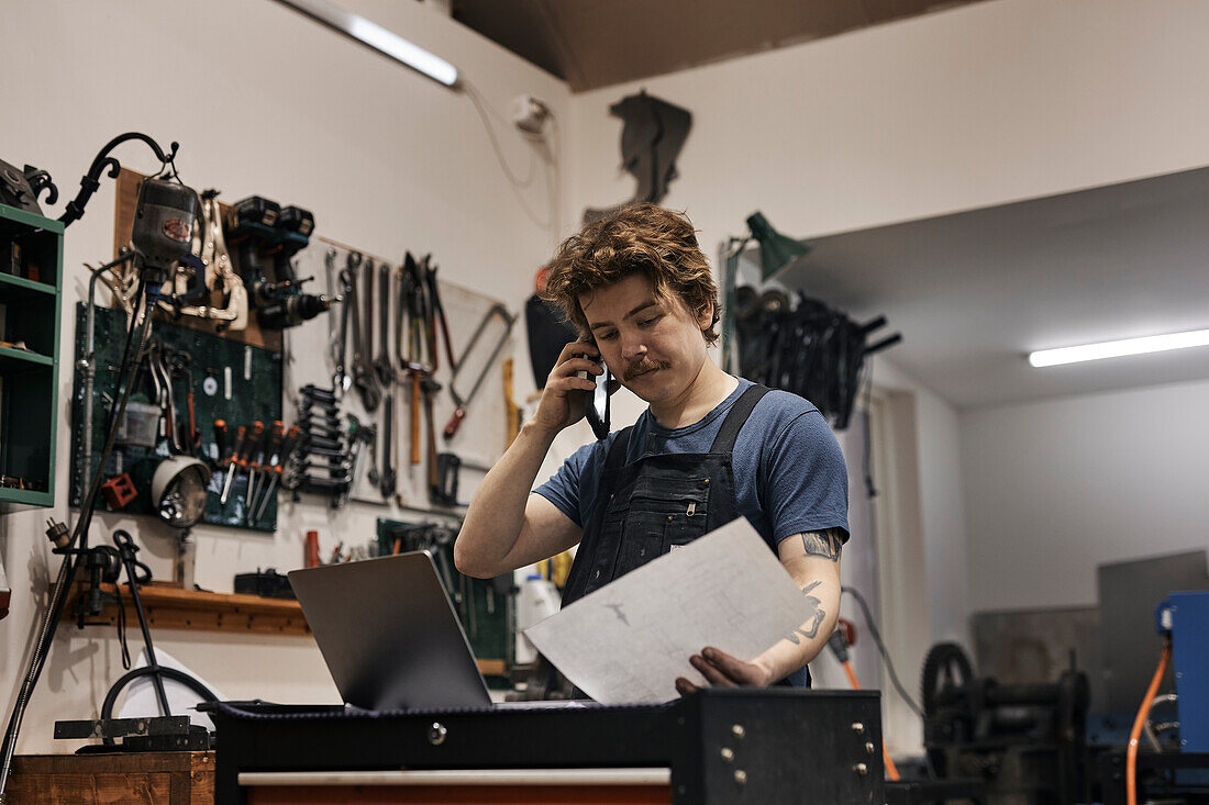 Blacksmith working with laptop and documents in his workshop