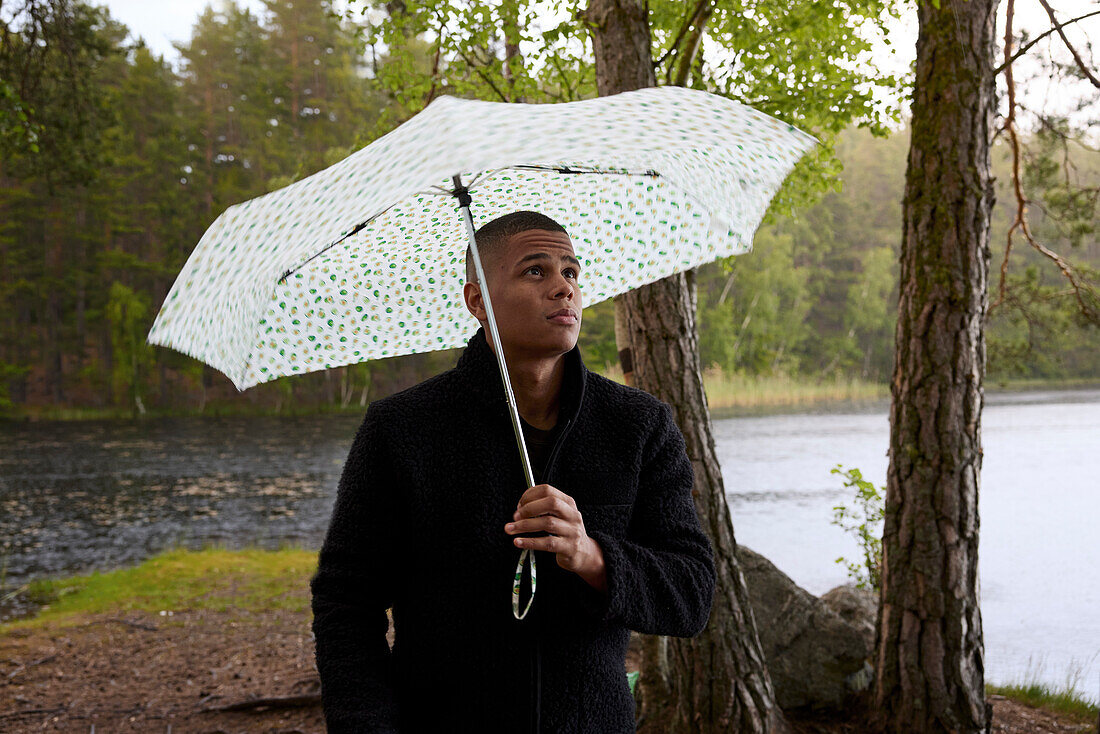 Young man holding umbrella at lake