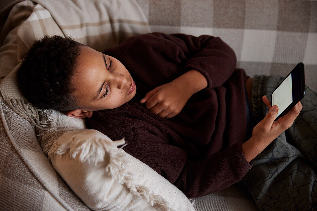 Boy lying on sofa and using phone