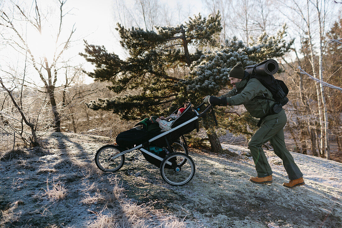 Mann schiebt Kinderwagen im Winter bergauf