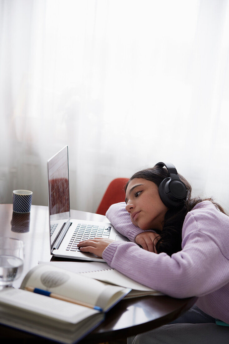 Girl doing homework with laptop at dining table