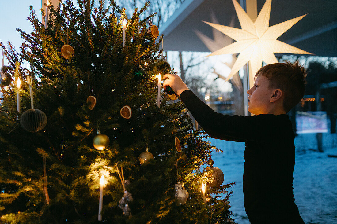 Junge schmückt Weihnachtsbaum zu Hause