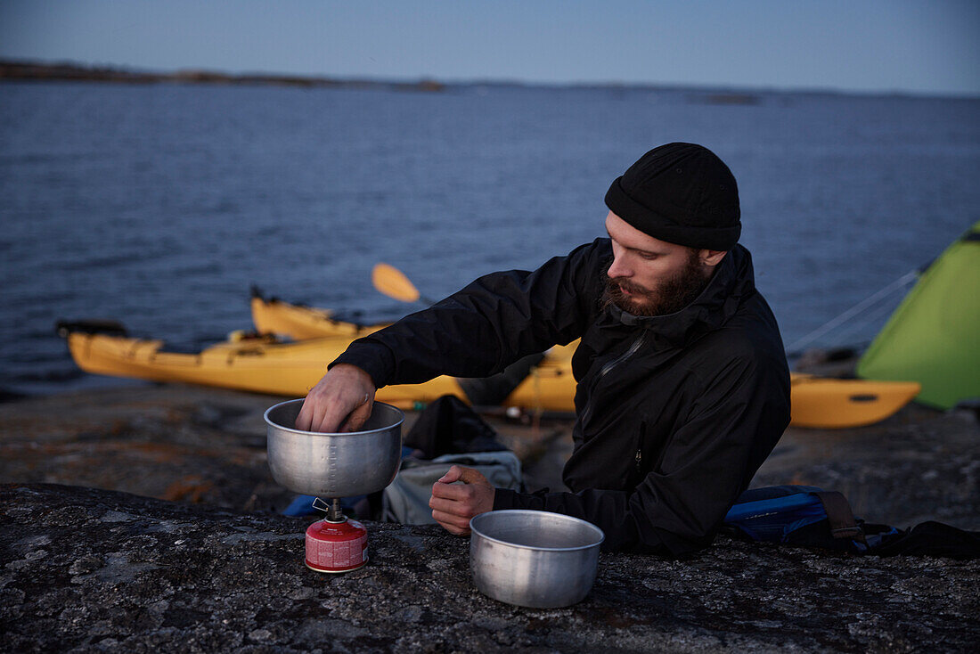 Mann bereitet Essen auf dem Meer zu, Kajaks im Hintergrund