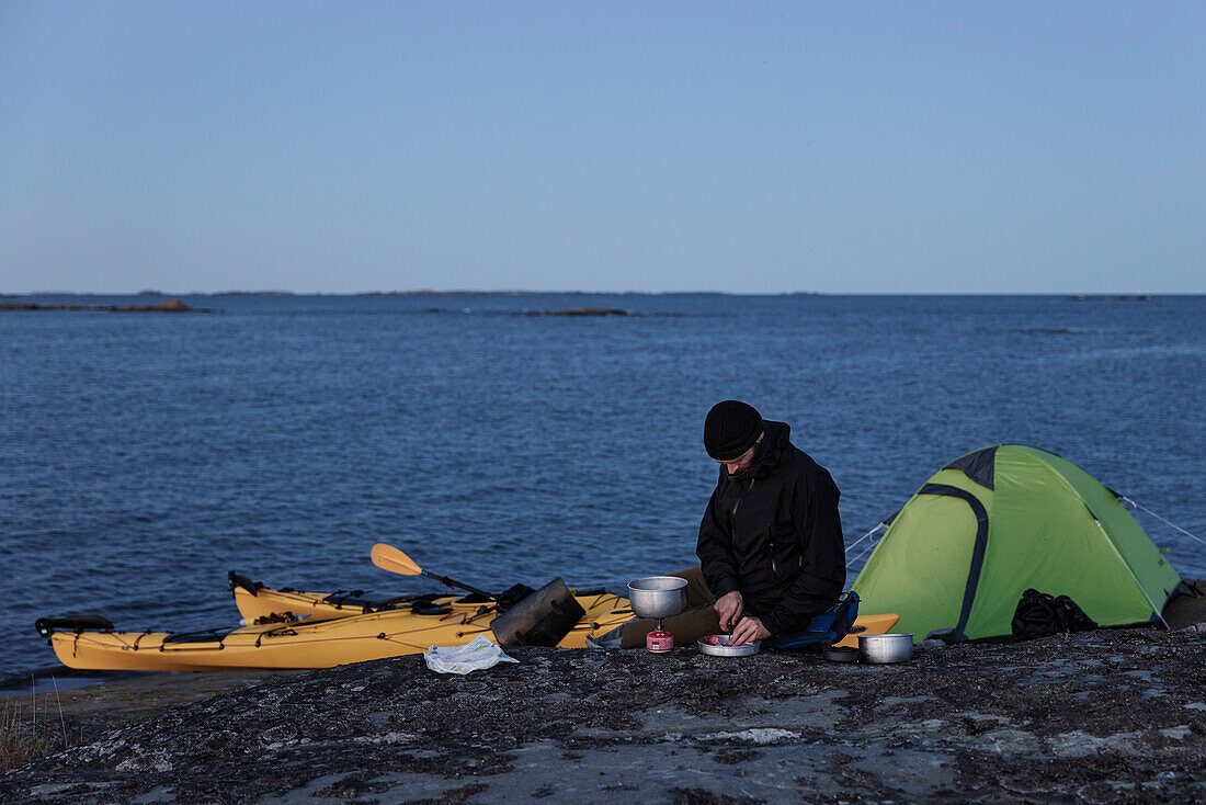 Man preparing food at sea, kayaks in background
