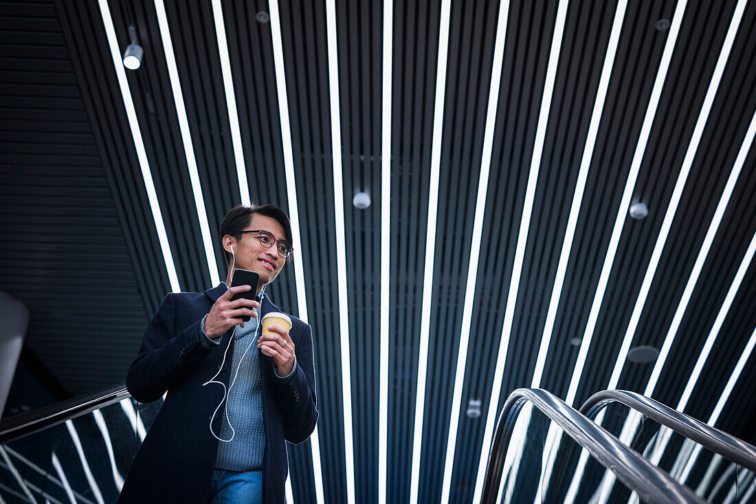 Handsome man with smartphone and paper cup on escalator